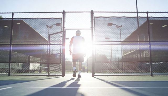 Backlit athlete walking through tennis court gate at sunrise with dramatic lens flare