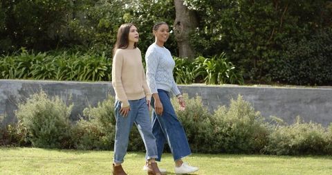 Diverse female friends strolling through green garden wearing sweaters and jeans