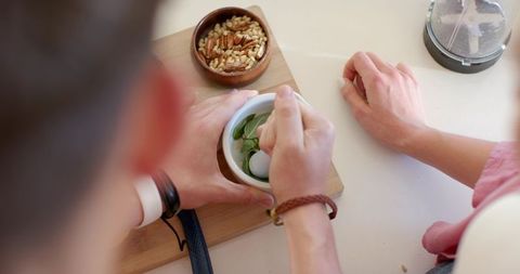 Teen male and woman grinding fresh herbs with mortar and pestle for homemade sauce