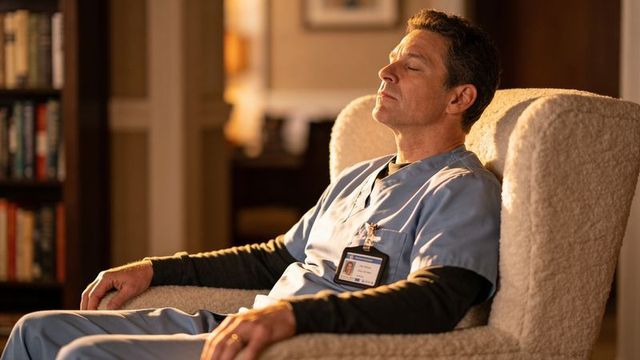 Male medical worker resting in armchair wearing blue scrubs and id badge, calm break moment