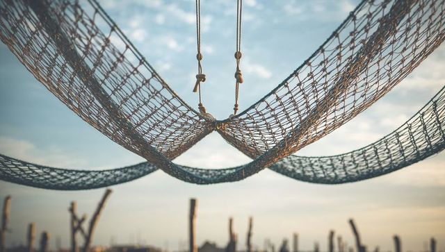 Hanging woven rope nets curving under golden-hour light at waterfront with knots and beads