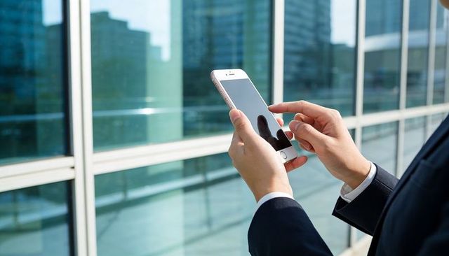 Business professional tapping smartphone near glass facade on urban office terrace