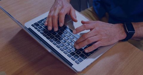 Typing adult male hands on silver laptop keyboard wearing smartwatch on wooden desk