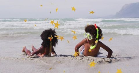 Siblings playing on sandy beach wearing neon snorkel mask and gold star confetti