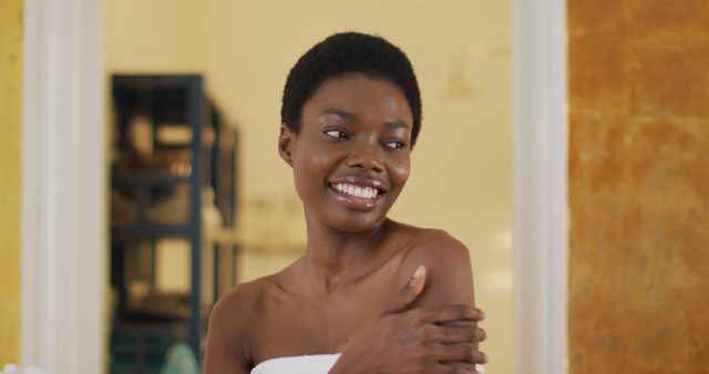Woman smiling joyfully while practicing self care at home. Ideal for wellness, skincare, and lifestyle themes. Use for articles or campaigns promoting personal care routines, relaxation tips, and positive self-image.