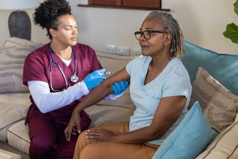 Nurse administering vaccine to senior african american woman at home