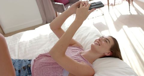 Teen Girl Relaxing on Bed with Smartphone in Sunny Bedroom