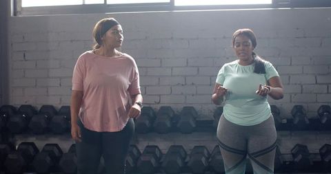 Two diverse women training in industrial gym wearing activewear and fitness trackers