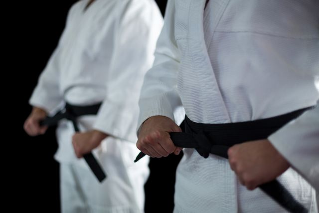 Two karate fighters in traditional white uniforms and black belts are standing in a focused stance against a black background. This image can be used for promoting martial arts classes, illustrating articles on self-defense, or showcasing the discipline and focus required in martial arts training.