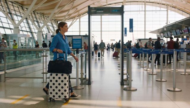 Woman walking through airport terminal pulling polka dot suitcase carrying duffel in blue shirt