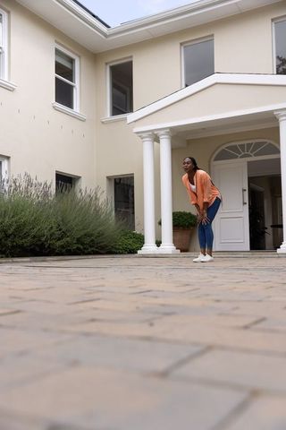 African american woman leaning on knees at elegant home entrance with columns and driveway