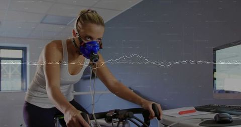 Female athlete undergoing metabolic test, cycling on ergometer while wearing respiratory mask in lab