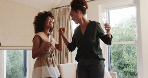 Joyful Female Partners Dancing with Champagne at Home Celebration