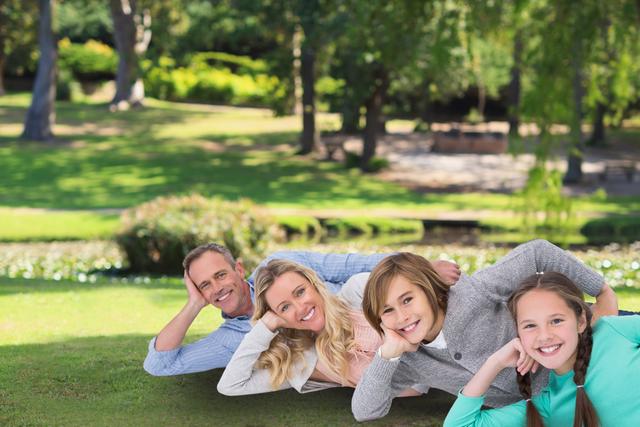 Family of four enjoying time together laying on grass in a park. Ideal for ads promoting family time, outdoor activities, and healthy living. Can also be used for articles on parenting, work-life balance, and family well-being.