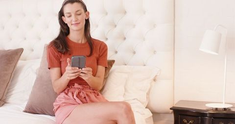 Woman Relaxing on Bed Using Smartphone in Cozy Bedroom