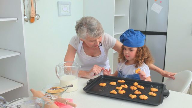 Family time in a home kitchen where a grandmother and her granddaughter are engaging in a joyful baking experience. The picture captures a heartwarming moment of bonding through cooking, ideal for illustrating parenting blogs, cooking magazines, and family-oriented content.