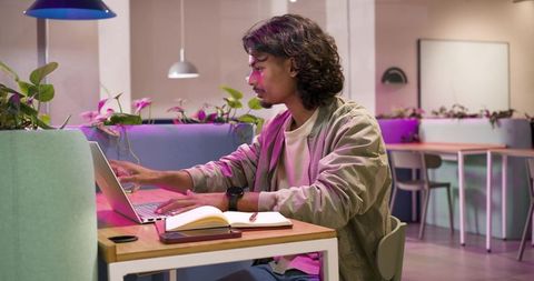African american young man working on laptop in modern coworking space with pastel lighting