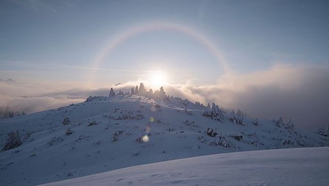 Sun Halo Over Snowy Alpine Ridge at Sunrise with Windcarved Cornices and Mist
