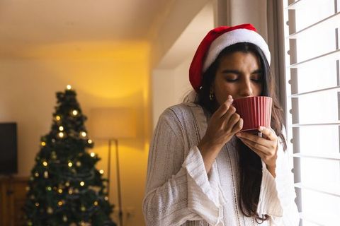 Woman in Santa Hat Enjoying Warm Drink Near Christmas Tree