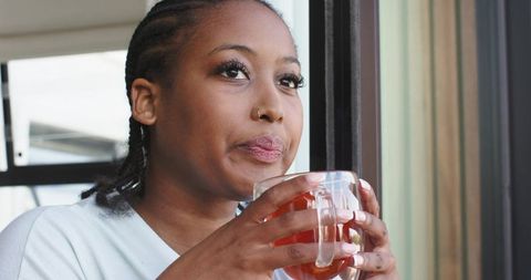 Contemplating African American woman sipping tea on balcony in bright minimalist interior