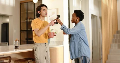 Pointing while holding coffee mug and sharing smartphone in bright modern kitchen