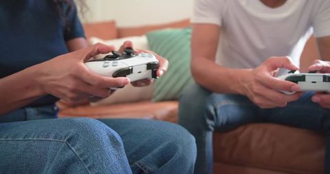 African american couple playing video games on leather couch with white controllers