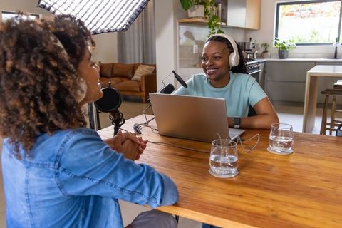 African american women co-hosts recording podcast in bright home kitchen with laptop mics