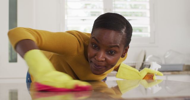 This image features a smiling woman wearing yellow gloves while wiping a kitchen counter. Ideal for use in articles about housekeeping tips, cleaning services, hygiene practices, and domestic chores. Suitable for blogs, advertisements, and informational content on hygiene and home maintenance.