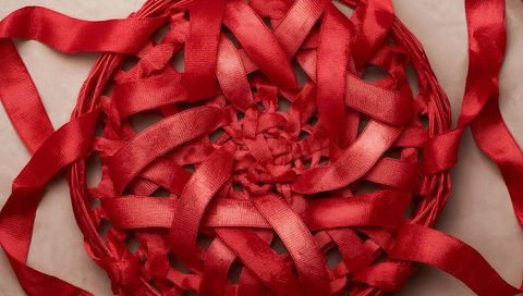 Woven red satin ribbon medallion displaying braided core and glossy loose tails