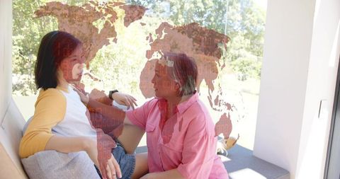 Mother supporting adult daughter on sunlit window seat with global map overlay
