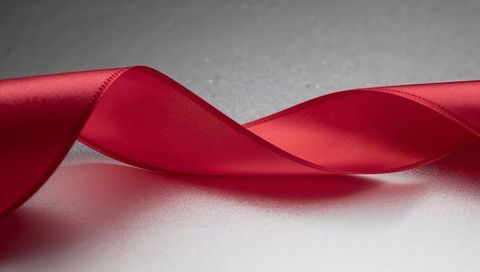 Flowing red satin ribbon forming elegant s-curve with stitched edges on neutral surface