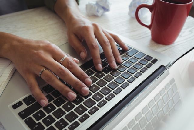 Cropped hands of businesswoman using laptop on desk in office