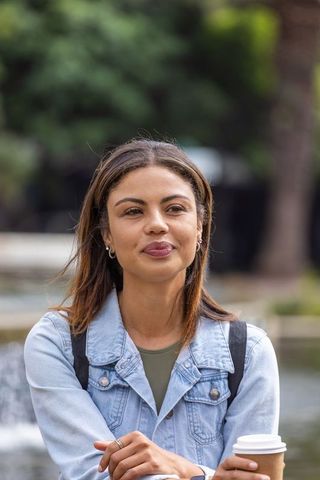 African american woman holding coffee at urban park fountain wearing denim jacket