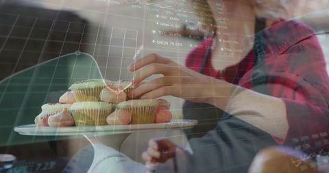 Home baker arranging frosted cupcakes with stock market overlay and cozy kitchen vibe