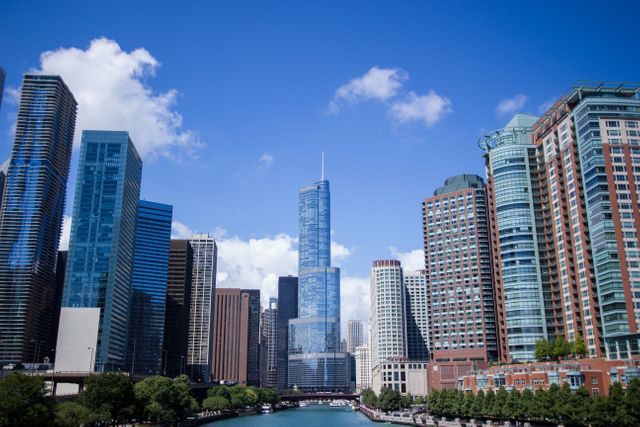 Tall modern buildings form Chicago's iconic skyline. The clear sky and sunny weather highlight the towering skyscrapers and urban landscape, with a river beautifully winding through the cityscape. Ideal for use in advertising, travel guides, postcards, and presentations focusing on urban development or tourism.