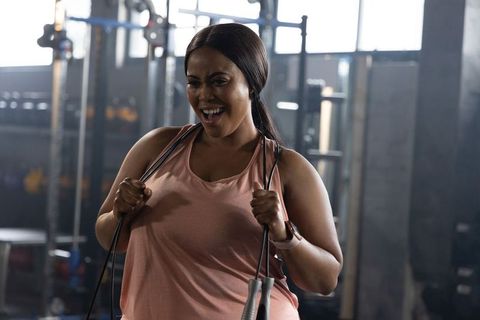 Confident african american woman smiling and jump roping while wearing fitness tracker in gym