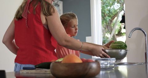 Mother and daughter washing lettuce at kitchen sink preparing healthy meal together