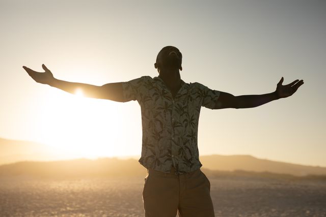African American man standing on a beach with his arms outstretched, sun in the background. Free time and vacation. 