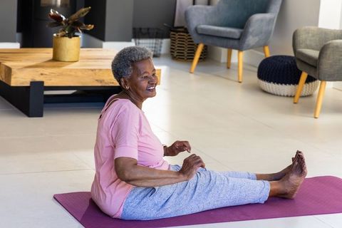 Senior african woman practicing gentle yoga and stretching on purple mat in bright living room