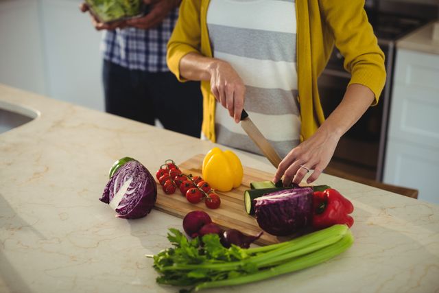 Couple chopping fresh vegetables together in a modern kitchen. Ideal for use in articles or advertisements related to healthy eating, cooking at home, lifestyle blogs, and culinary tutorials. Highlights teamwork and domestic life.