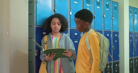 African american teens reading notebook by blue lockers in school hallway
