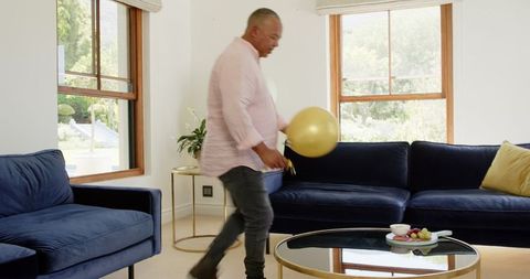 Senior Man Decorating Modern Living Room with Balloons for Party