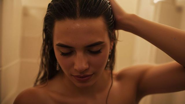 Woman adjusting wet hair in warm shower closeup with water droplets and soft light