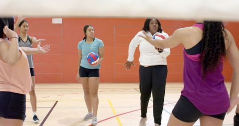 Female volleyball team practicing indoors with coach directing drills and teamwork training