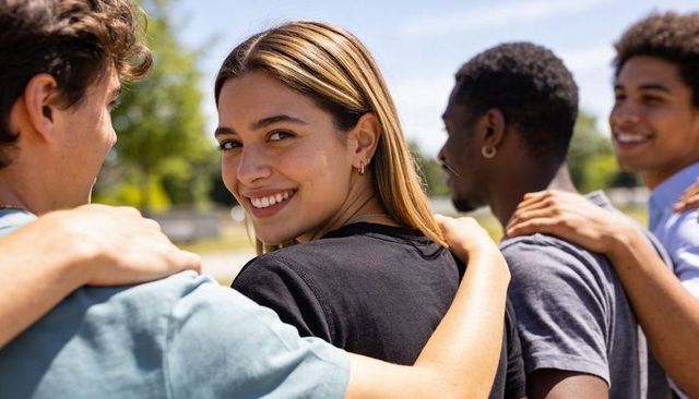Smiling teen looking back while friends linking arms in sunny park