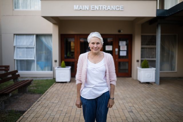 Portrait of smiling senior woman standing against house entrance