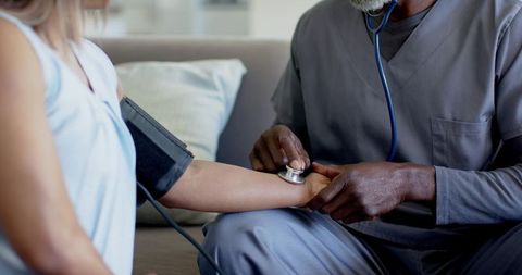 African american clinician checking blood pressure of mature female patient at home
