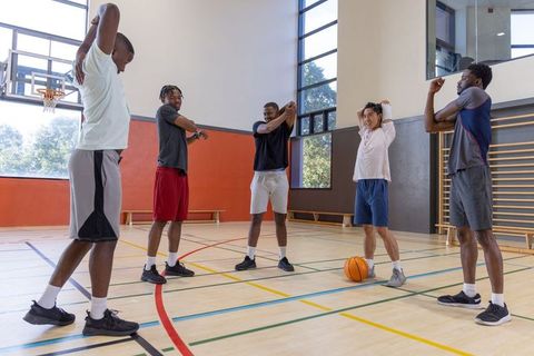 Diverse male teammates warming up on indoor gym court before basketball practice