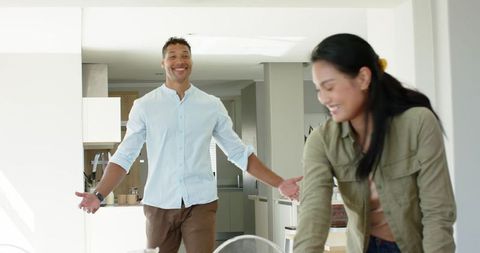 Diverse couple smiling and arranging dining table in sunlit modern open-plan homey kitchen