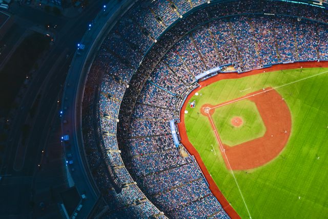 Aerial view captures crowded baseball stadium during a night game. Suitable for use in sports event promotion, advertisements, editorial content on professional baseball games, stadium architecture features, or publications about sporting events and competition ambiance.